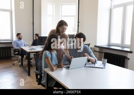 Diverse group of cheerful employees sharing computer at office table Stock Photo
