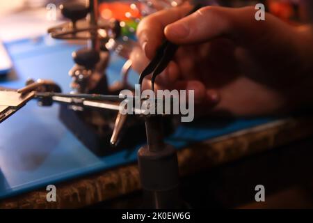 Defocus male hand with tweezers. Work with a soldering iron. Microelectronics device. Close-up hands of a service worker repairing modern smartphone. Stock Photo