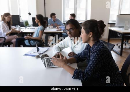 Two serious Indian colleagues talking at work table, sharing laptop Stock Photo