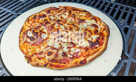 Pizza cooked on a pizza stone in a barbeque. Stock Photo