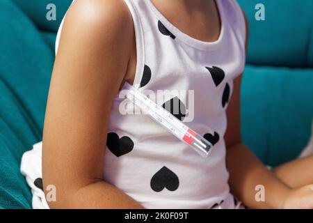 Girl with fever on the sofa with thermometer in her armpit Stock Photo