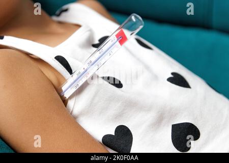 Girl with fever on the sofa with thermometer in her armpit Stock Photo