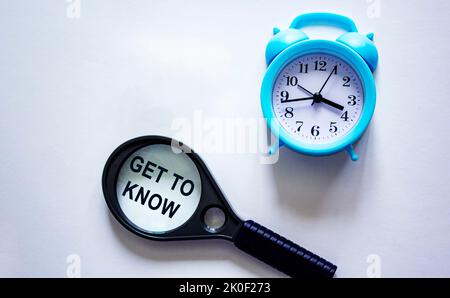 Get to know written on a magnifying glass and a white background with a clock. Stock Photo