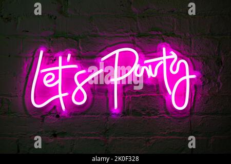 Lets party pink glowing neon sign banner on brick wall Stock Photo