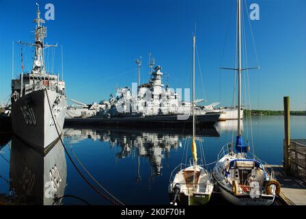 The Battleship USS Massachusetts and destroyer USS Joseph P Kennedy are reflected int he still water of Fall River Stock Photo