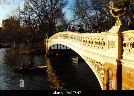 Two friends take a rowboat on the lake on an early spring day, passing under the Bow Bridge in Central Park, New York City Stock Photo