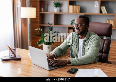 Cheerful confident mature african american businessman in glasses and casual working on laptop in home office Stock Photo