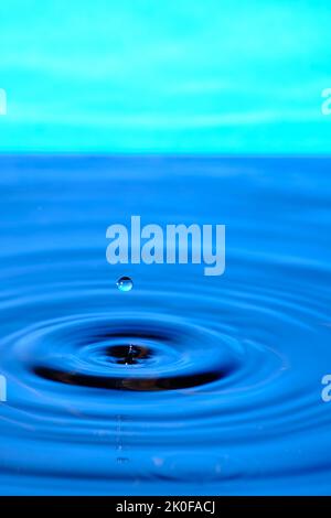 Splash drop of water with diverging water circles, on blue background Stock Photo