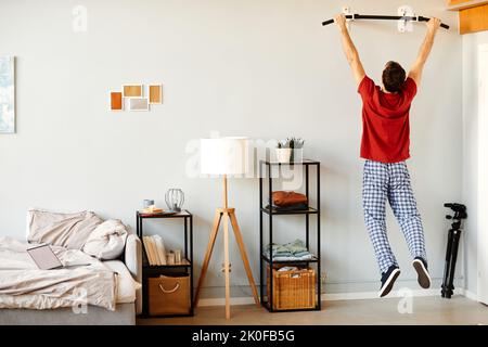 Rear view of young man doing exercises on bar during sport training in the morning at home Stock Photo