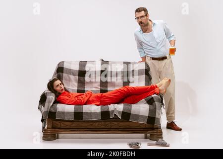 Portrait of emotive couple watching horror movie together. Woman lying in pyjama on sofa, man drinking beer Stock Photo