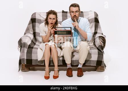 Portrait of concentrated couple, man and woman sitting on sofa and listening to the news on radio Stock Photo