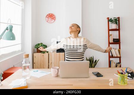 Smiling mid adult woman stretching body while working on laptop at home office Stock Photo