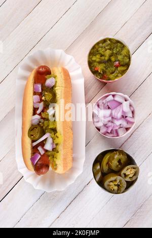 Overhead still life of a summer picnic table with a hot dog smothered in relish onions and jalapenos. Three cups of condiments are lined up next to th Stock Photo