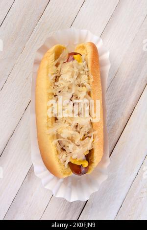 High angle shot of a Kraut Dog. A grilled hot dog on a bun with mustard and sauerkraut on a rustic white wood picnic table. Stock Photo