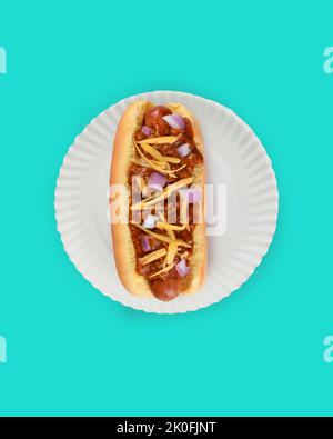 Flat Lay Hot Dog in Bun Still Life. Fankfurter in bun with Chili, Cheese and onions on a white paper plate on teal background with copy space. Stock Photo