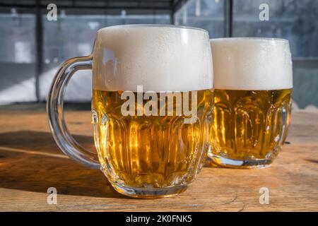 Two mugs of light beer with foam on a wooden table Stock Photo