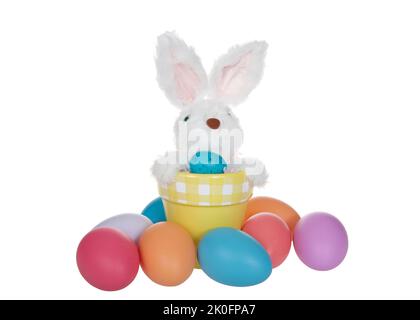 Fuzzy bunny sticking out of a yellow terra cotta pot surrounded by colorful Easter eggs isolated on white. Stock Photo