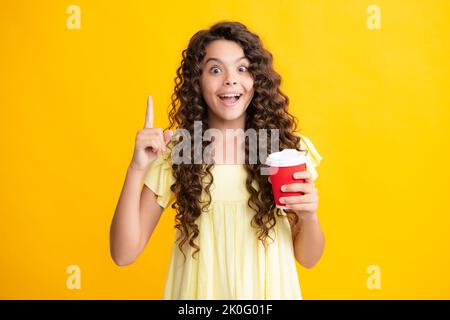 Teenager child with coffee cup isolated on yellow studio background. Girl drinking take away beverage. Excited teenager, glad amazed and overjoyed Stock Photo