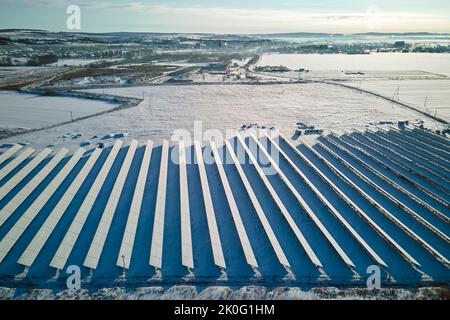 Aerial view of sustainable electrical power plant with solar photovoltaic panels covered with snow in winter for producing clean energy. Concept of
