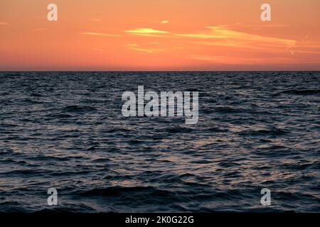Dramatic bright red sky at ocean sunset, soft evening clouds over sea dark water Stock Photo