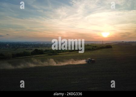 Tractor spraying fertilizers with insecticide herbicide chemicals on agricultural field at sunset Stock Photo