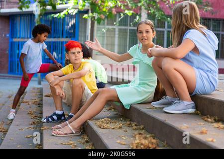Positive tweenagers friendly blabbing while sitting on steps outdoors Stock Photo