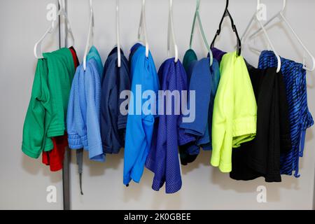 Many different colors of men’s gym shorts and sport shorts hanging on hangers in a closet closeup. A variety of different color sport shorts in closet Stock Photo