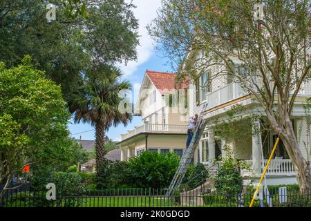 NEW ORLEANS, LA, USA  - SEPTEMBER 7, 2022: Two workers on ladders repairing an historic house on St. Charles Avenue in Uptown neighborhood Stock Photo