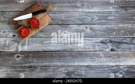 Single ripe organic tomato sliced in half with cutting knife plus server on rustic wood table in flat lay format Stock Photo