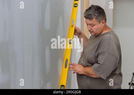 With the aid of a level, the employee checks the equalization of the drywall before it is painted Stock Photo