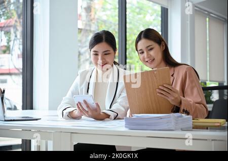 Two beautiful and attractive young Asian businesswomen or female accountants working together in the office. Teamwork concept Stock Photo