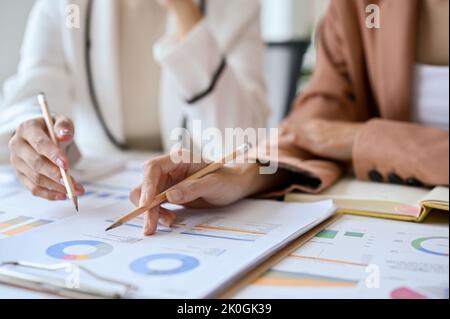 cropped and close-up hands, Two businesswomen or financial analysts working together, analyzing and brainstorming on their financial report. Stock Photo