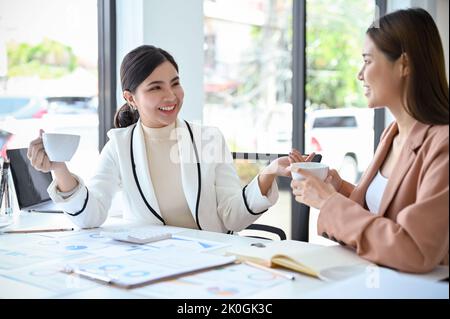 Two beautiful and happy young Asian businesswomen or office employees enjoy talking chatting during the office break in the office. Stock Photo