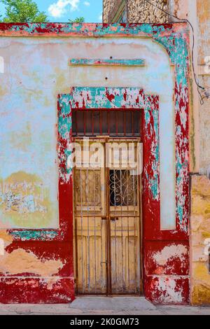 Colorful grunge around broken down door with wrought iron accents and locked bars in front on street in Merida Yucatan Mexico Stock Photo