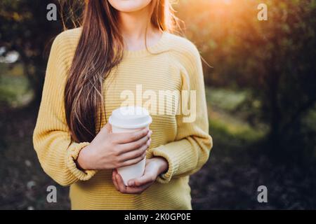 Unrecognizable young girl wearing a yellow sweater and holding white coffee cup in the park. Autumn vibe Stock Photo