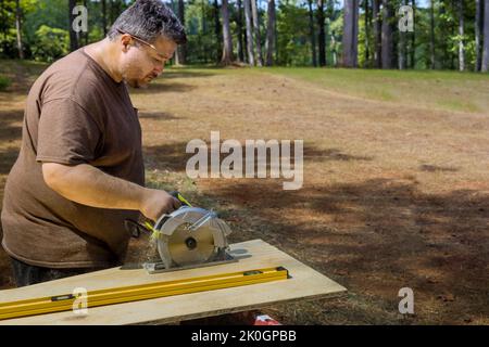 Using a circular saw in hand, the worker cuts plywood with the help of a circular saw held in his hands Stock Photo