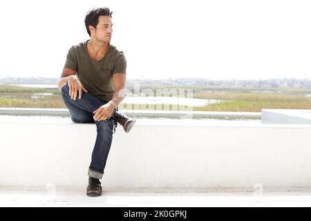 Feeling relaxed. A handsome young man looking thoughtful while sitting outside. Stock Photo