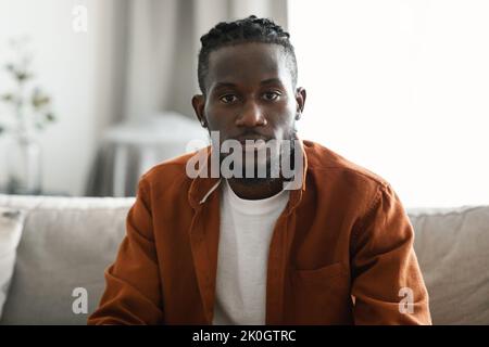 Portrait of african american guy sitting on couch in living room interior and looking at camera, headshot closeup Stock Photo
