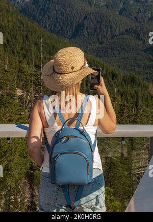 Young woman hiker doing selfie at the top of Squamish hike. Travel through Canada. Beautiful girl doing photos of landscape in trekking on the mountai Stock Photo