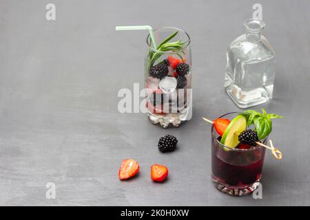 Ice, rosemary and berries in glass. Infused summer drink with blackberries and green basil in glass.  Water bottle. Strawberries and blackberries on t Stock Photo