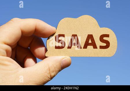 Against the background of the sky in the hands of a man, a figure of a cloud with the inscription - SaaS. Technology and business concept. Stock Photo