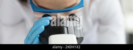 Woman doctor scientist looking through microscope in clinic Stock Photo
