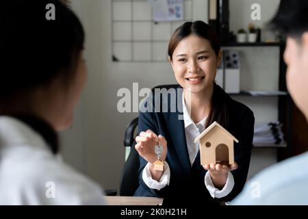 Happy family couple making purchase their first house, taking key from female realtor. View from behind the customers. Estate agency concept Stock Photo