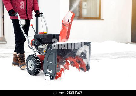 Closeup of red snow blower in action. Senior mature man outdoor in front of house using snowblower machine for removing snow on yard. Snow thrower in winter outside home. Young worker guy blowing snow Stock Photo