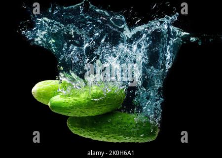Group of fresh cucumbers dropped in water with splashes isolated on black background. Stock Photo