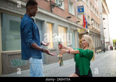 Blonde caucasian woman giving flowers to an african man in the street Stock Photo