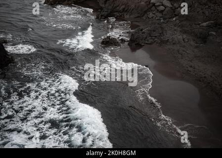 Black sand beach aerial view. Small volcanic rocks and graphic diagonal waves Stock Photo