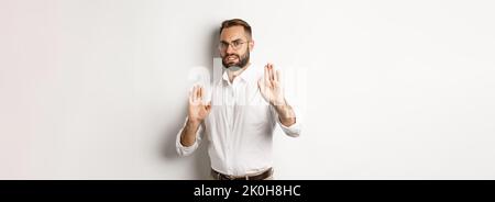 Displeased man rejecting something disturbing, showing stop sign and declining, cringe from aversion, standing over white background Stock Photo