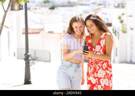 Happy tourists in a white town street checking smart phone on summer vacation Stock Photo