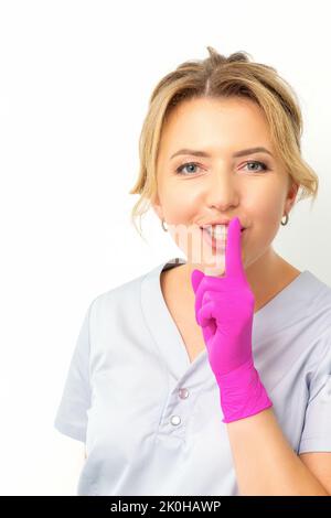 Young beautiful caucasian woman doctor, beautician doing silent gesture pressing his index finger to his lips isolated on white background Stock Photo